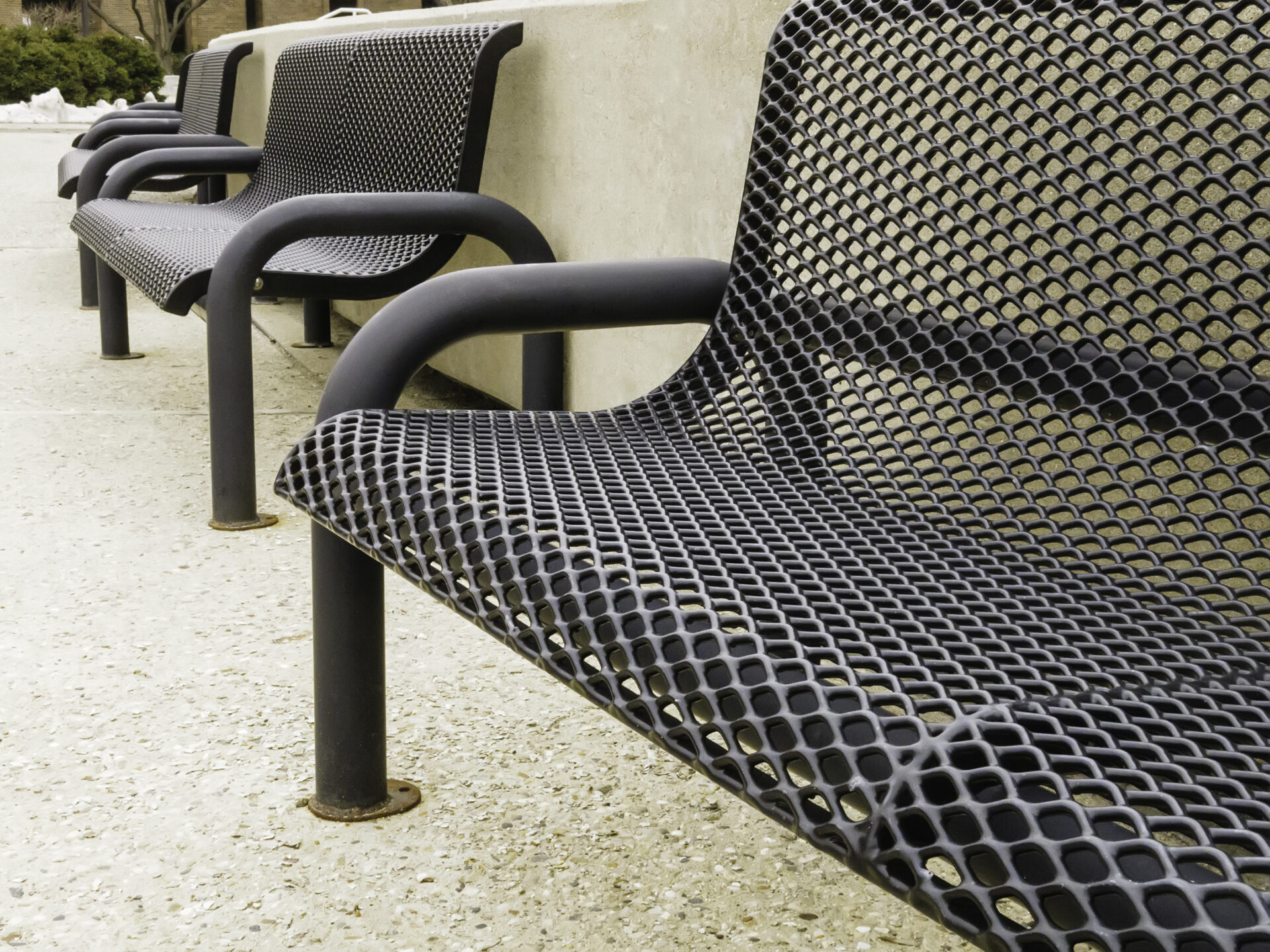 Row of vacant see-through metal benches on campus of community college.